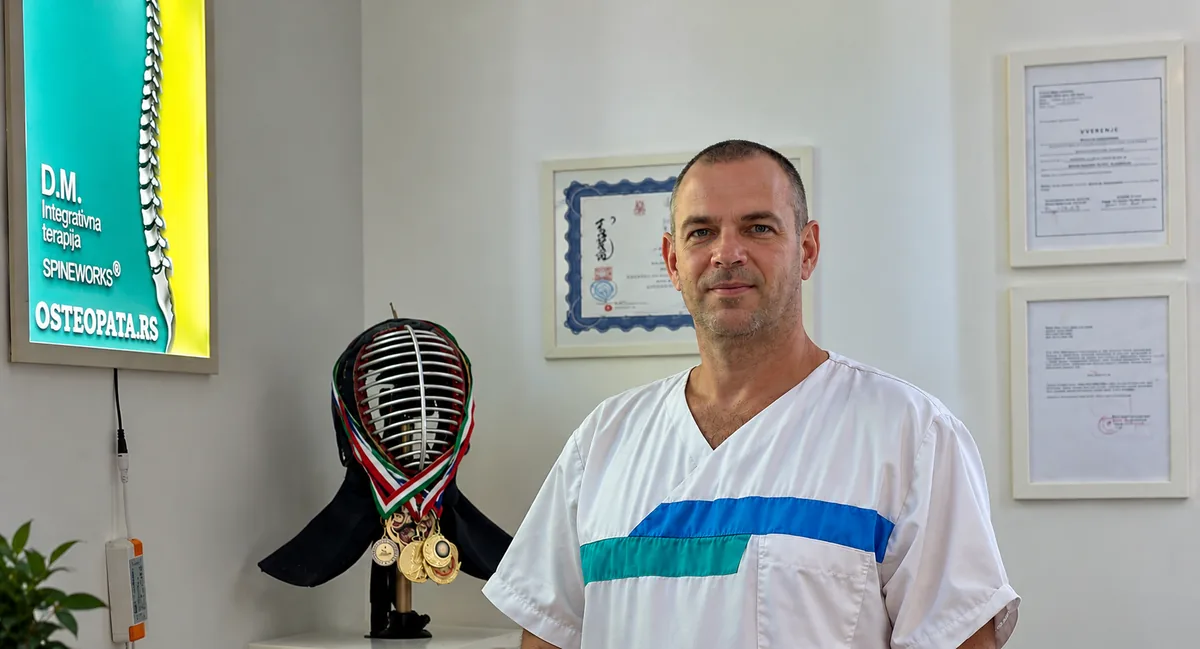 Dragan Mitrović u ordinaciji, pored kacige za borilačke veštine sa medaljama i uramljenih diploma
